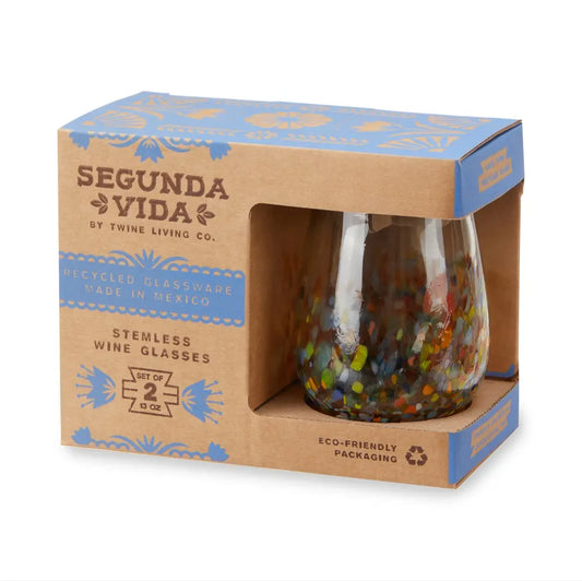 A boxed set of Segunda Vida recycled stemless wine glasses. The product is shown in its brown kraft paper packaging with blue decorative accents, featuring a clear window that displays the colorful recycled glass inside.